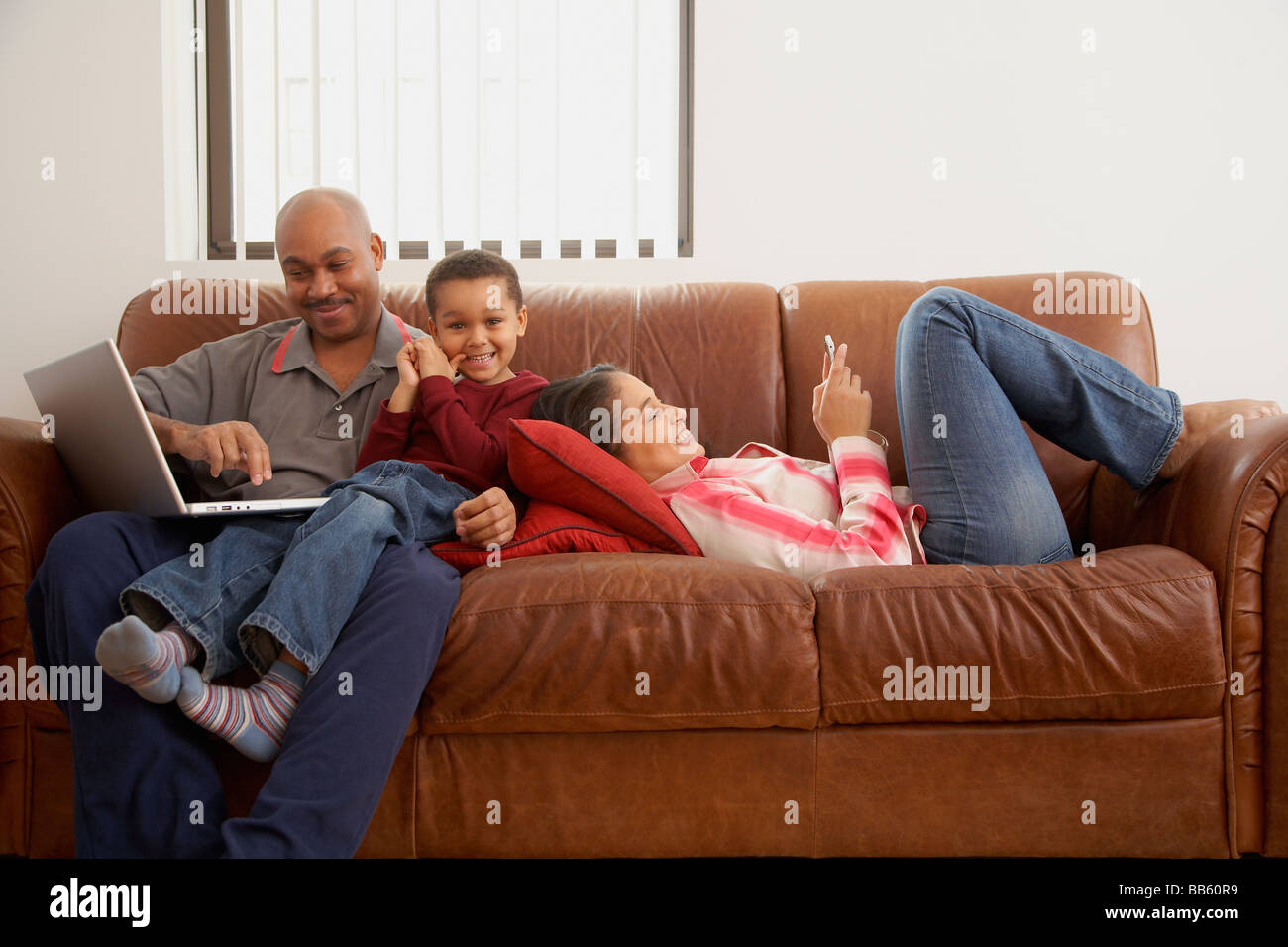 Antiguan man using laptop in living room with family Stock Photo