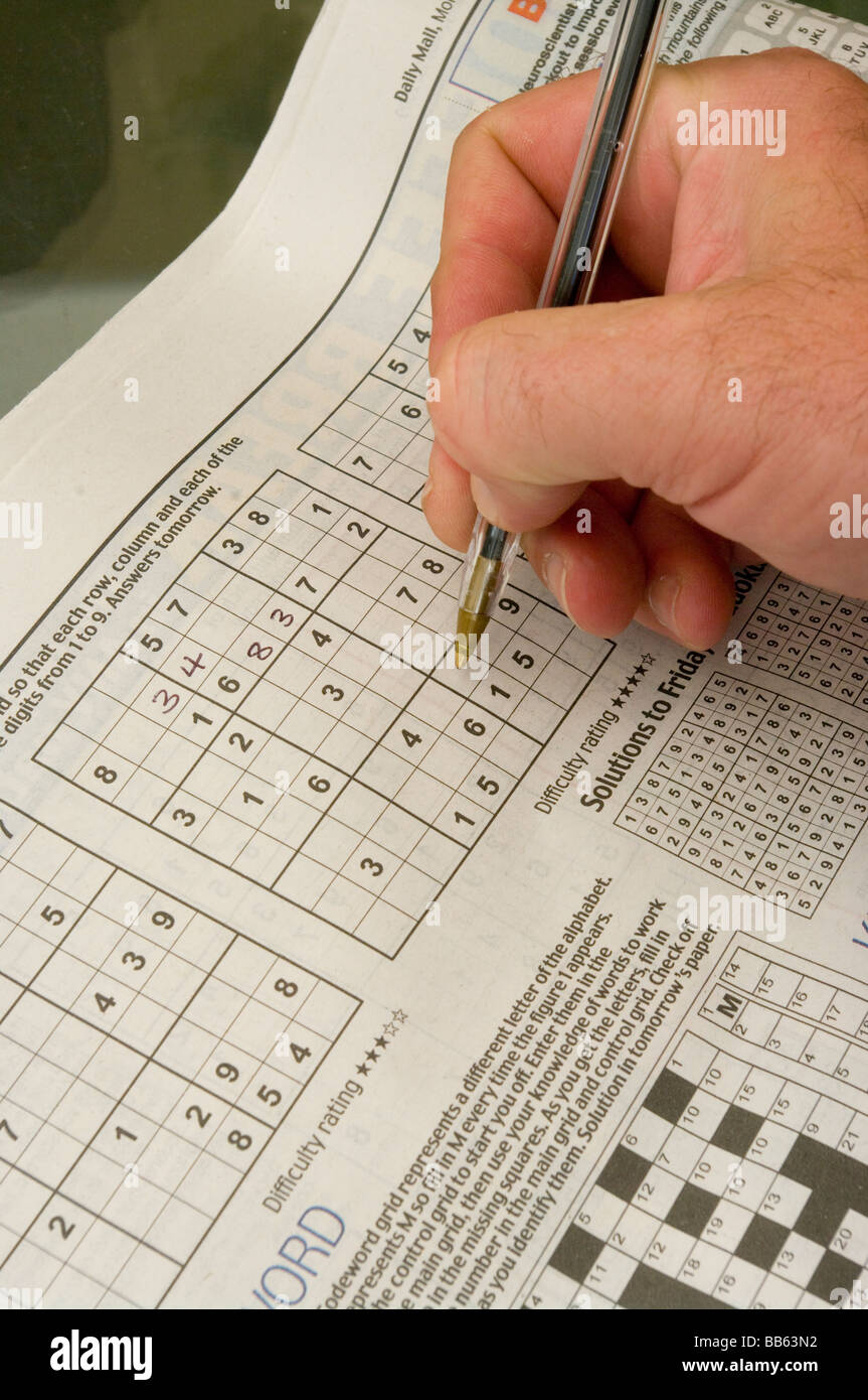 Mans Hand With A Pen Doing A Sudoku Puzzle in a Newspaper Stock Photo