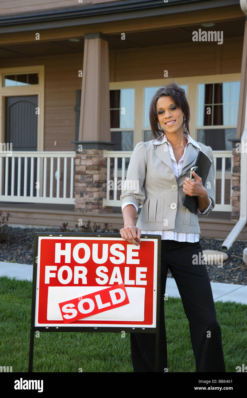 Realtor standing in front of home with SOLD sign Stock Photo