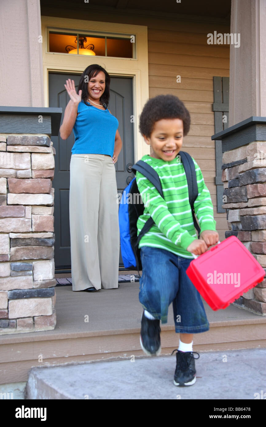 Mother on porch waves to child heading off to school Stock Photo