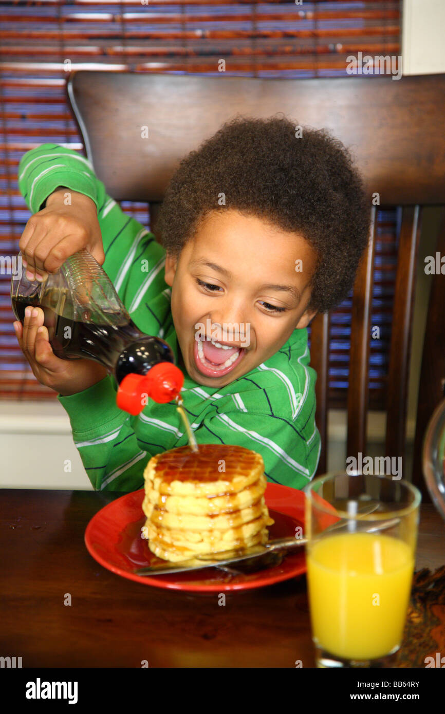 Young boy pours syrup on stack of waffles Stock Photo