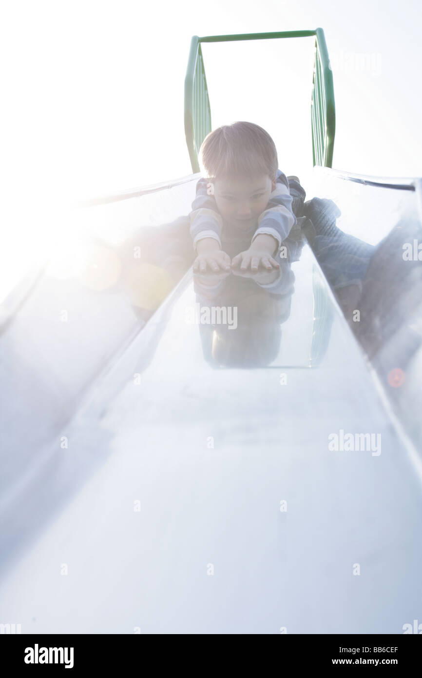 two year old boy at the top of a slide lying on his front head first Stock Photo