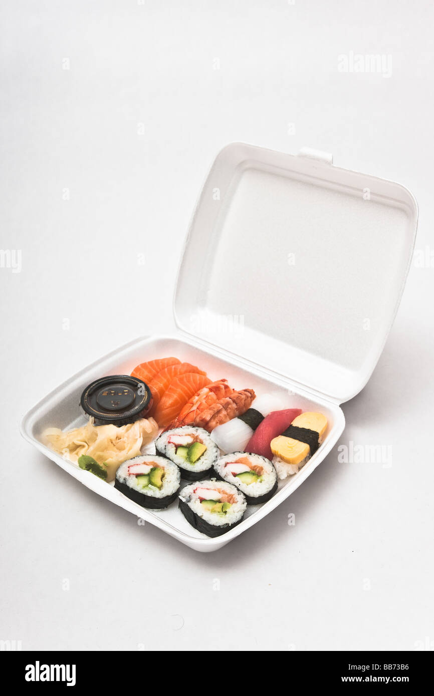 Styrofoam box with twelve pieces of take-out sushi and a cup of soy sauce, some ginger, and some wasabi. Stock Photo