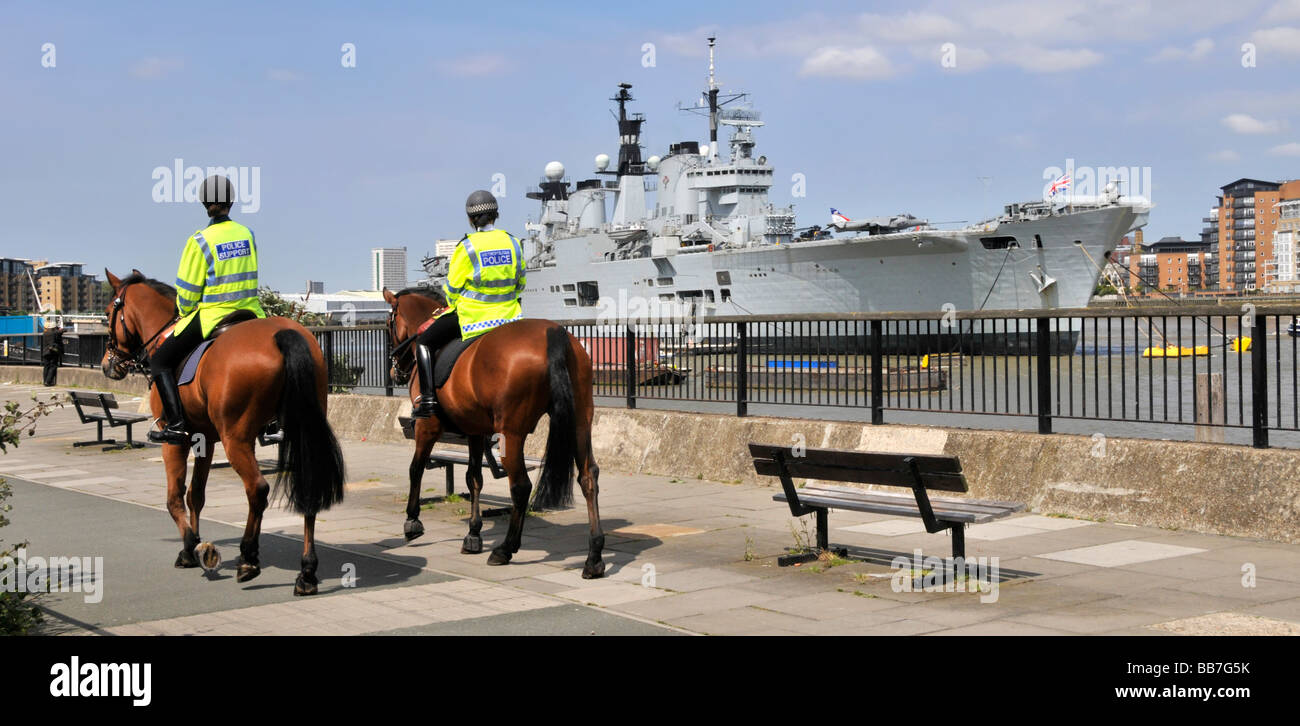 Royal Navy warship HMS Illustrious light aircraft carrier moored in River Thames Greenwich London passing mounted police patrol Stock Photo
