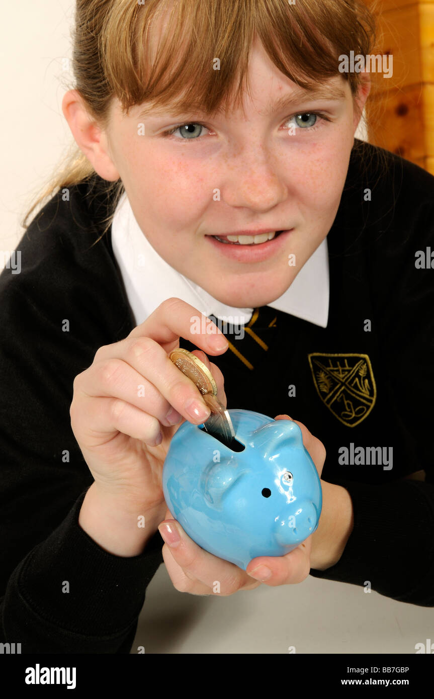 Young girl putting money into her blue coloured piggy bank saving for a ...