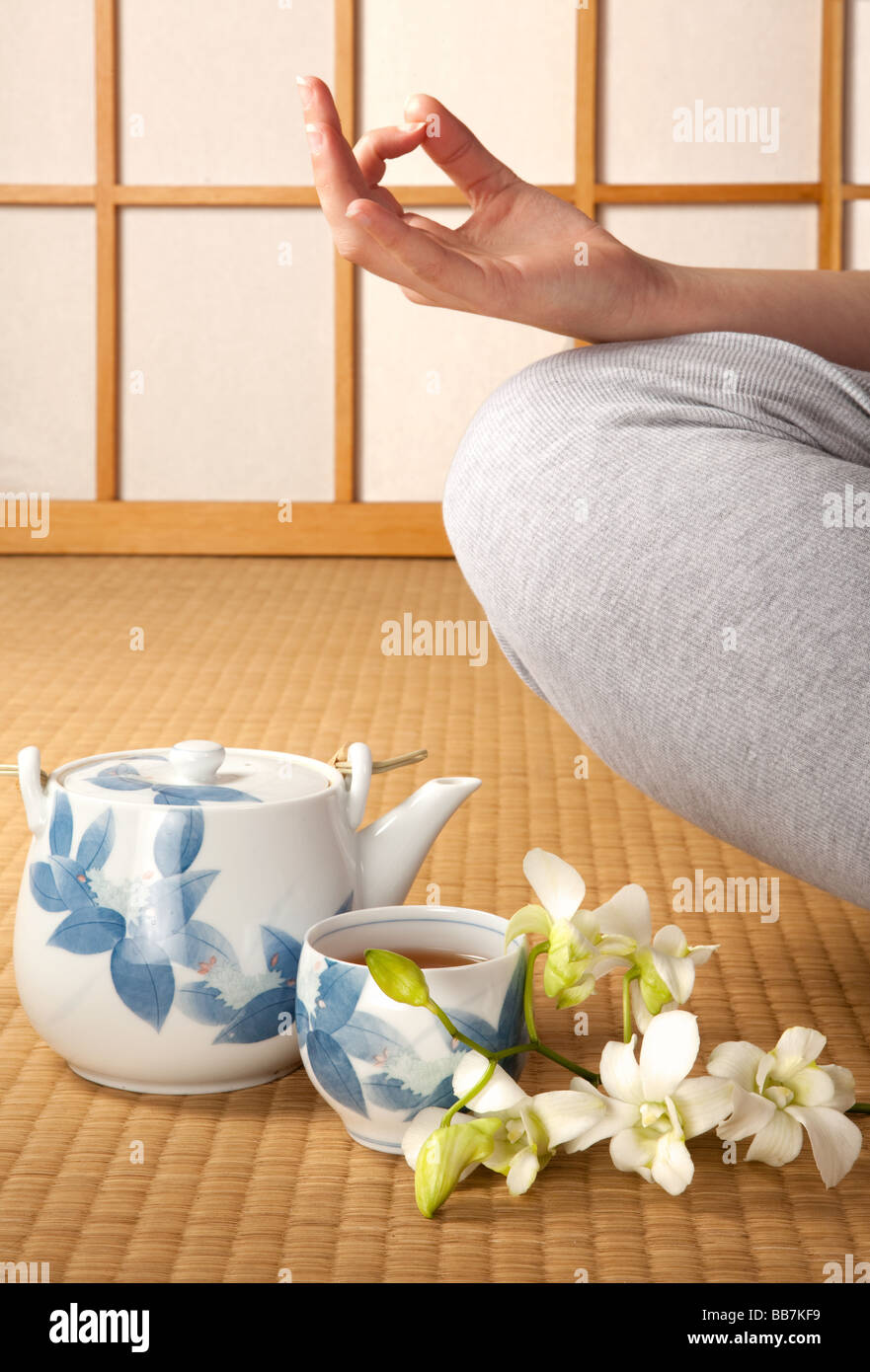 Meditating woman on japanese tatami mat with green tea and orchids Stock Photo