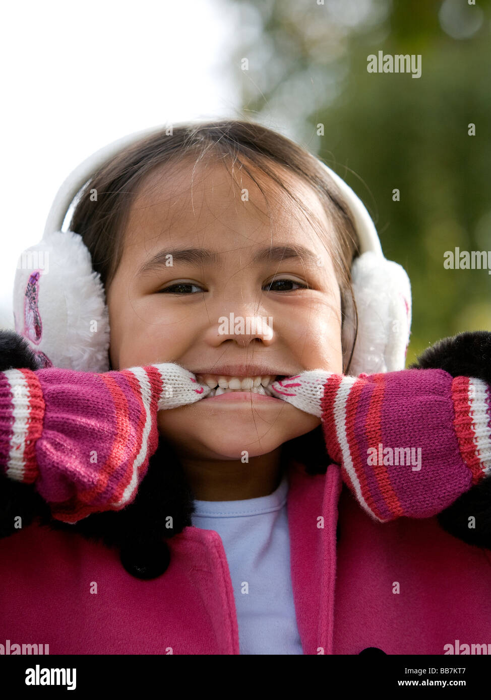 Young half-Thai girl wearing gloves and ear muffs pulls a face for the camera Stock Photo