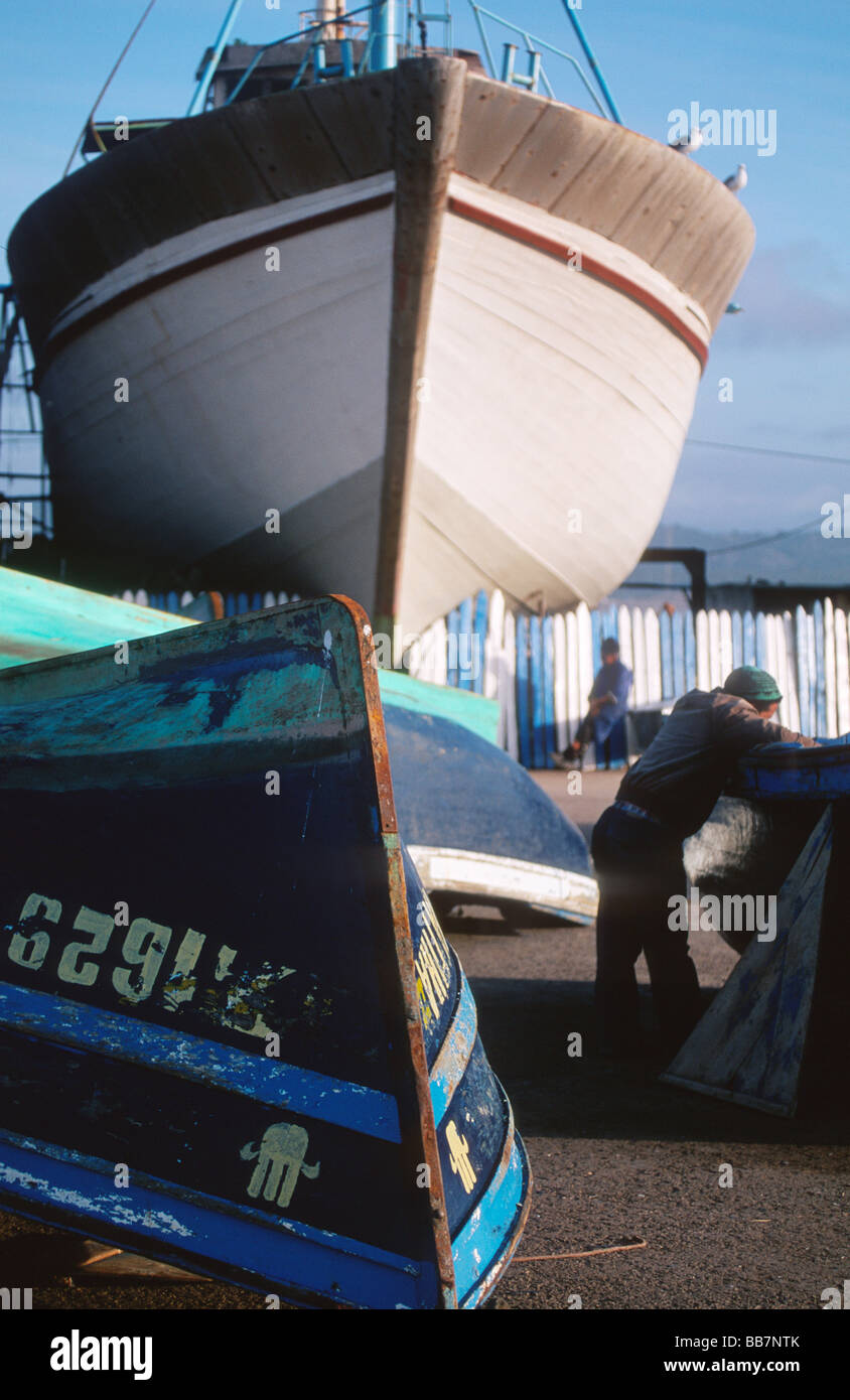 Fishing vessel and boats on dry dock with fishermen resting, port of Essaouira, Morocco Stock Photo