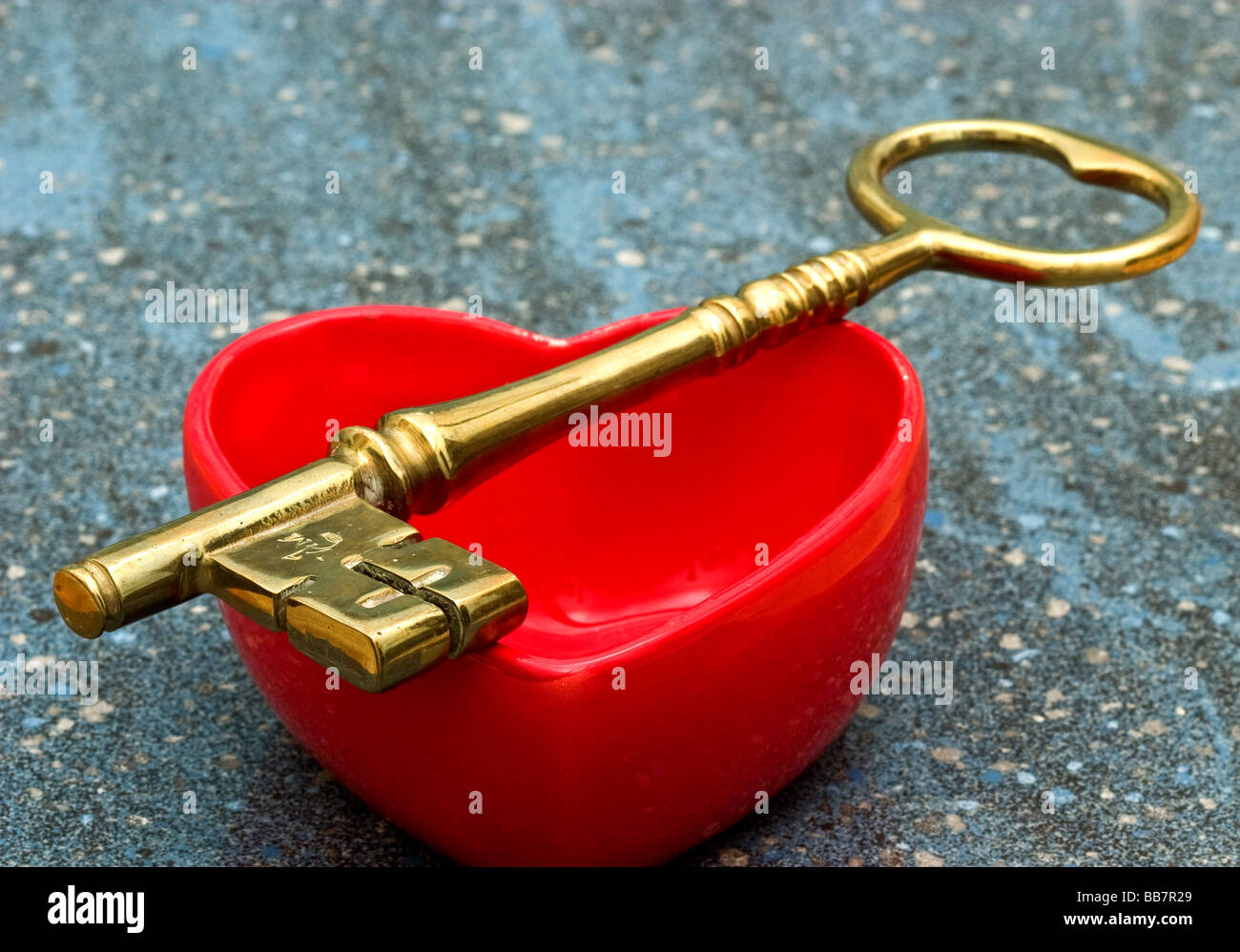 Large golden metallic key over a red heart shaped dish Stock Photo