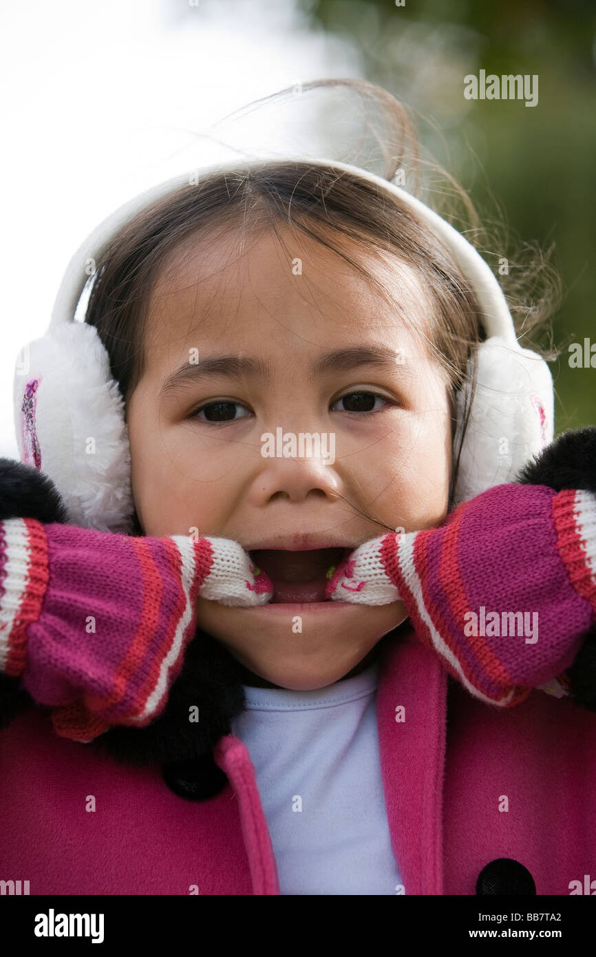Young half-Thai girl wearing gloves and ear muffs pulls a face for the camera Stock Photo