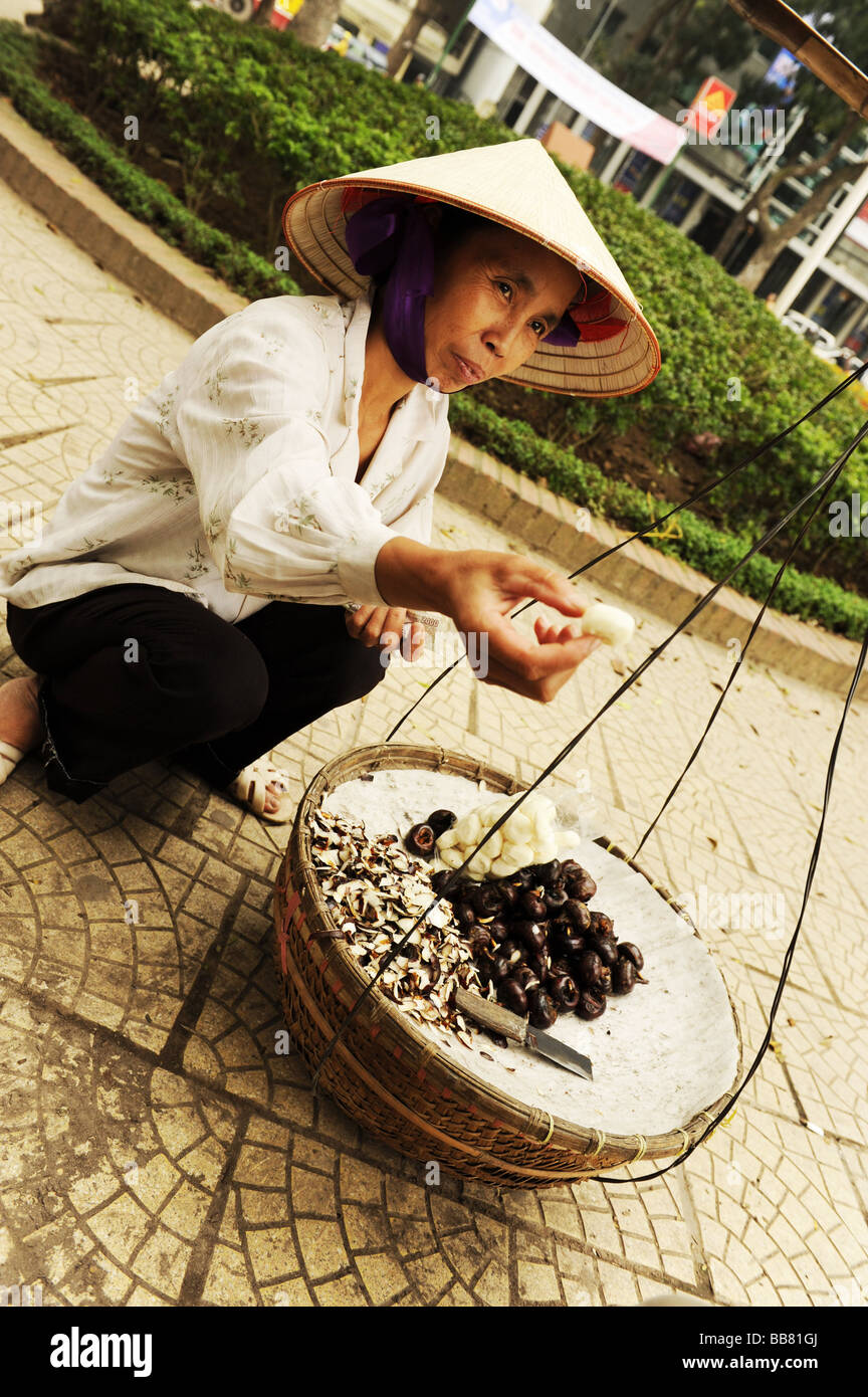 Street hawker giving waternut or matai or chinese water chestnut to test, old Quarter, Hanoi, Vitenam. Stock Photo