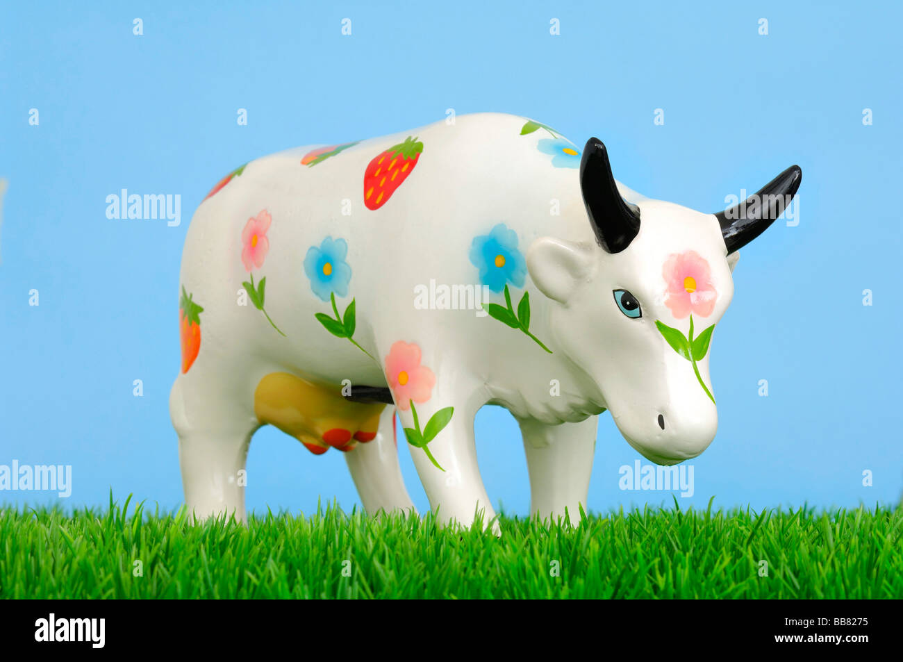 Ceramic cow with blossoms, piggy bank on grass Stock Photo