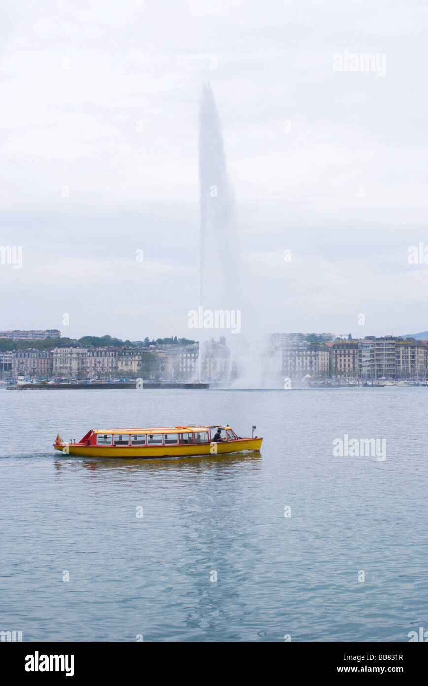 Yellow Taxi Boat Passes In Front Of Jet D'Eau Fountain in Lake Geneva Geneve Switzerland Stock Photo