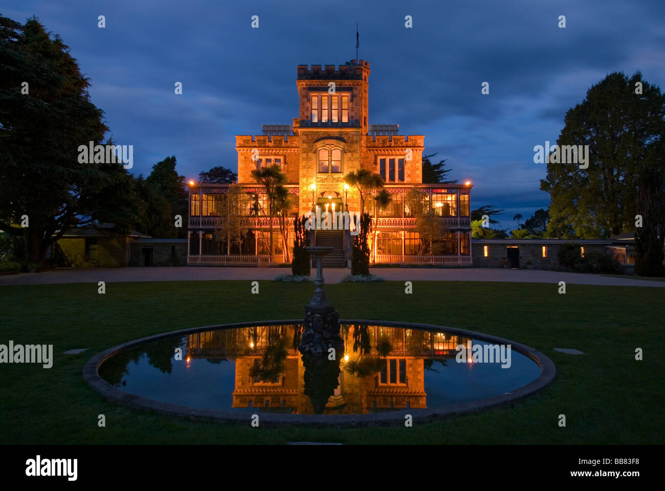 Larnach Castle on the Otago Peninsula and its reflexion in the pond of a fountain illuminated by floodlight, New Zealand Stock Photo