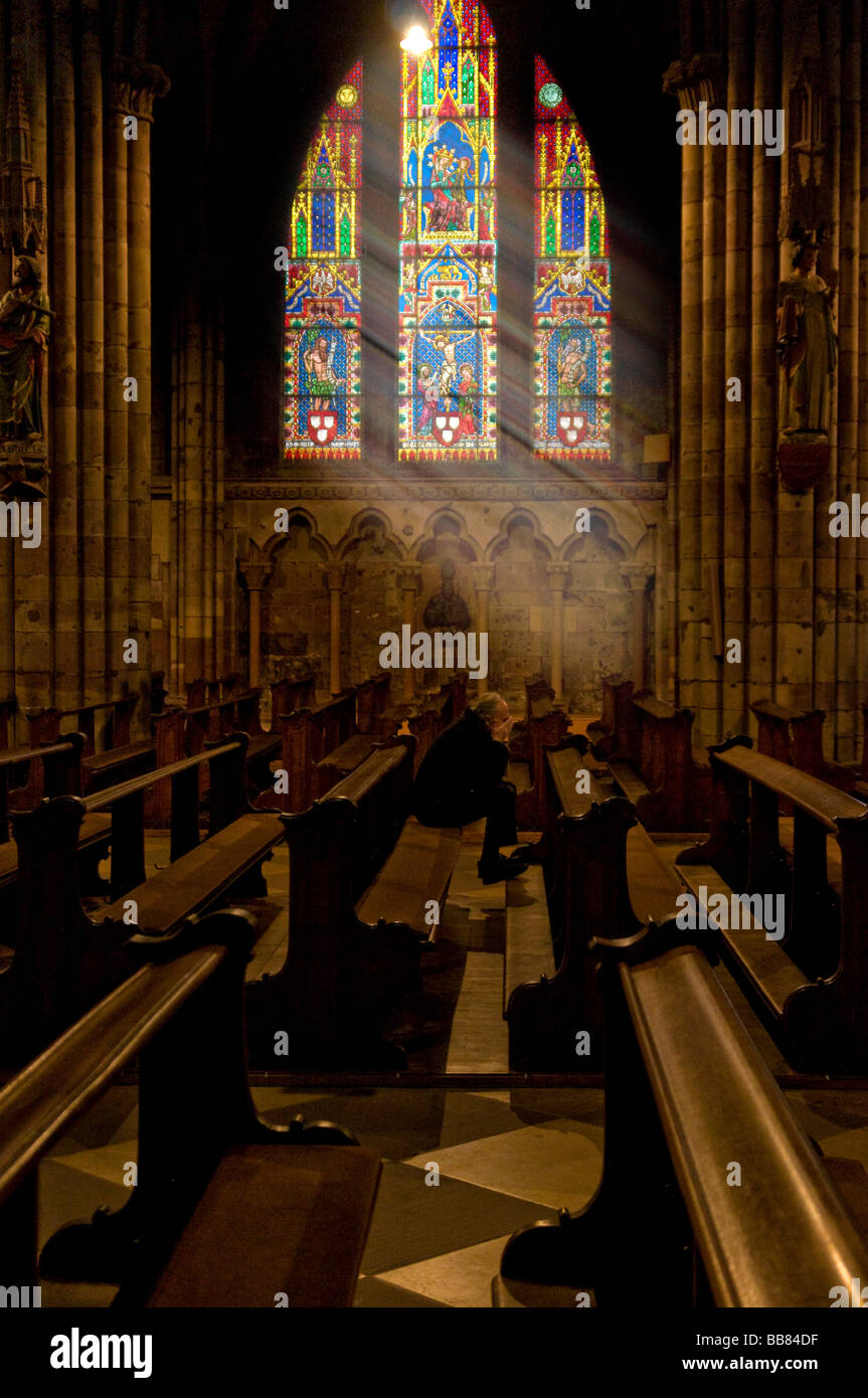 Freiburg Minster, interior, with sole man praying, shafts of sunlight shining through the colourful stained-glass window, Freib Stock Photo