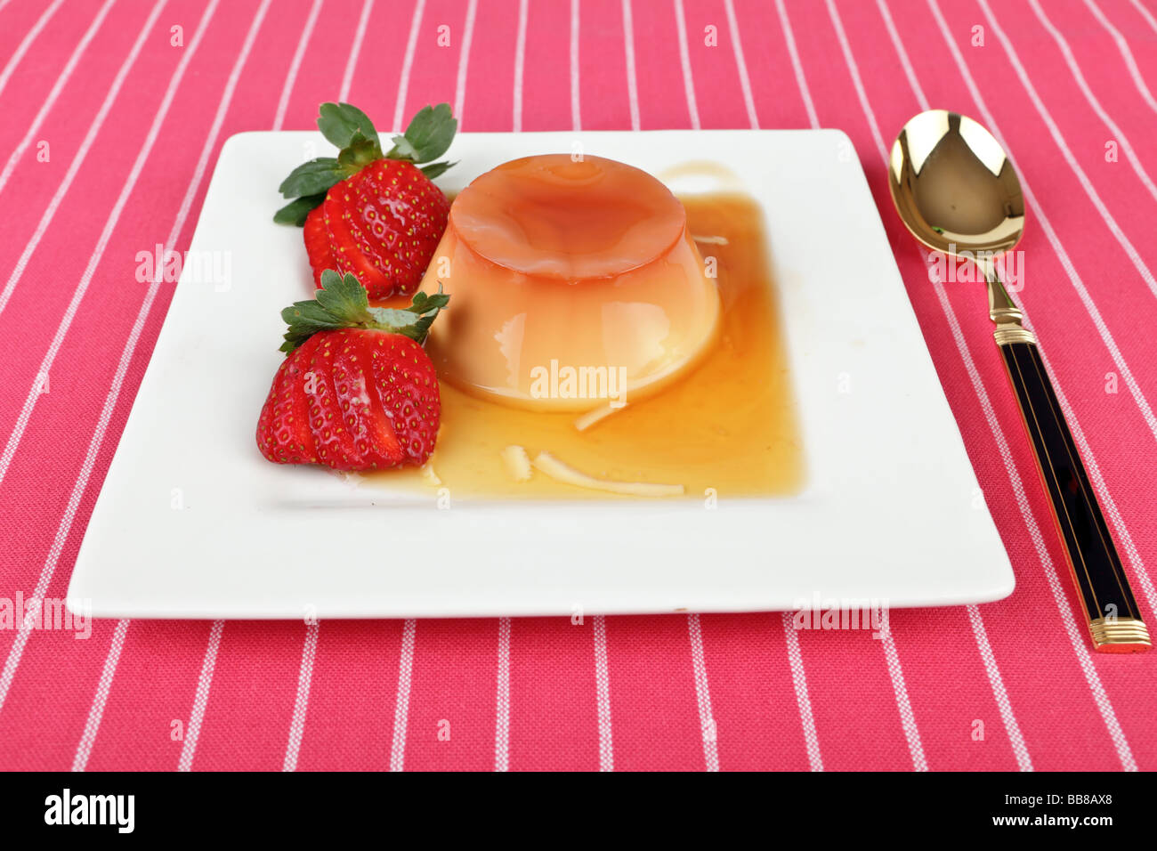 Creme caramel dessert with strawberries on aplate with spoon Stock Photo