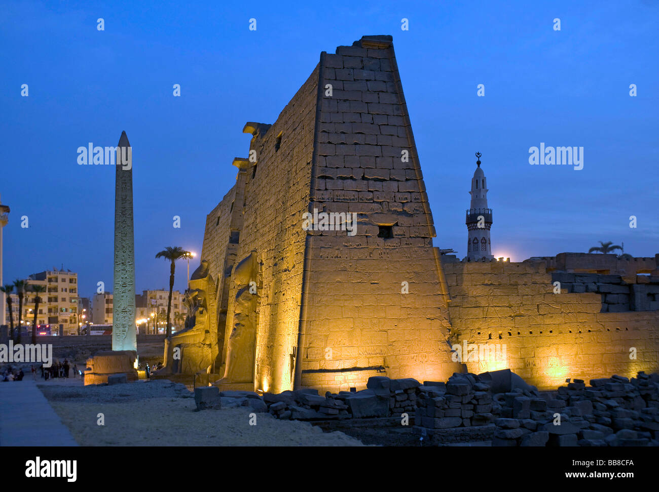 Pylon with figures and obelisk of Ramesses II illuminated in the evening, in front of a minaret, Luxor Temple, Luxor, Egypt, Af Stock Photo
