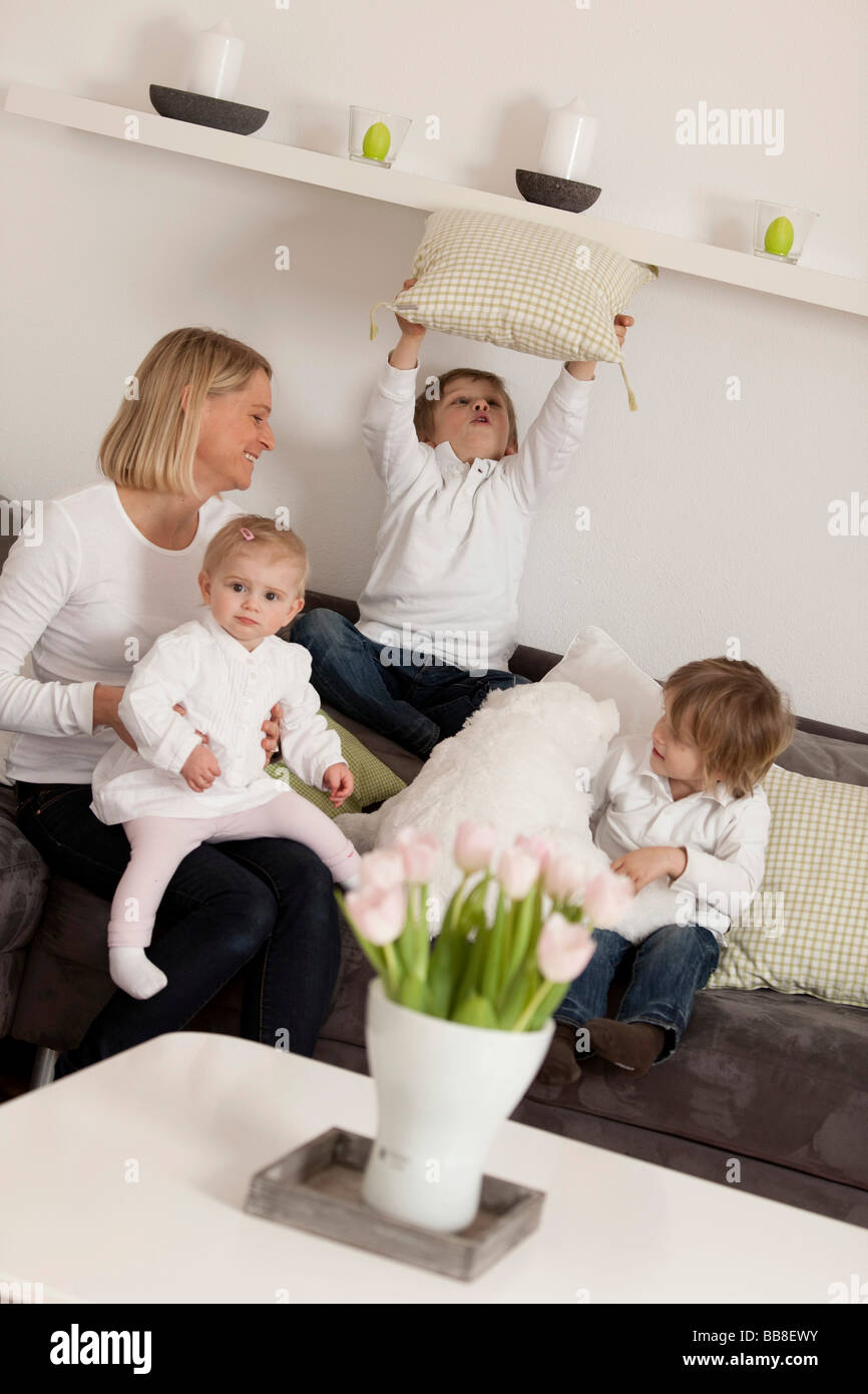 Mother and three children, 1, 3 and 6 years old, playing on the couch Stock Photo