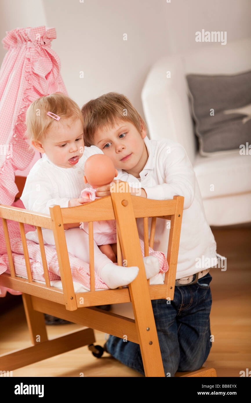 Boy, 6 years old, playing with his sister, 1 year old, holding a doll Stock Photo