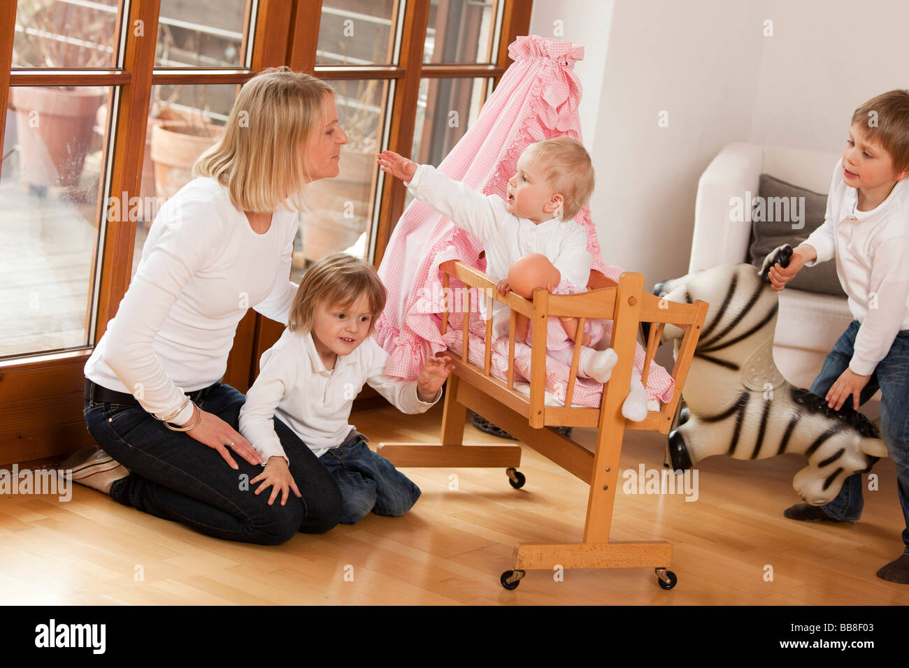 Mother with three children, 1, 3 and 6 years old, playing with a doll's pram Stock Photo