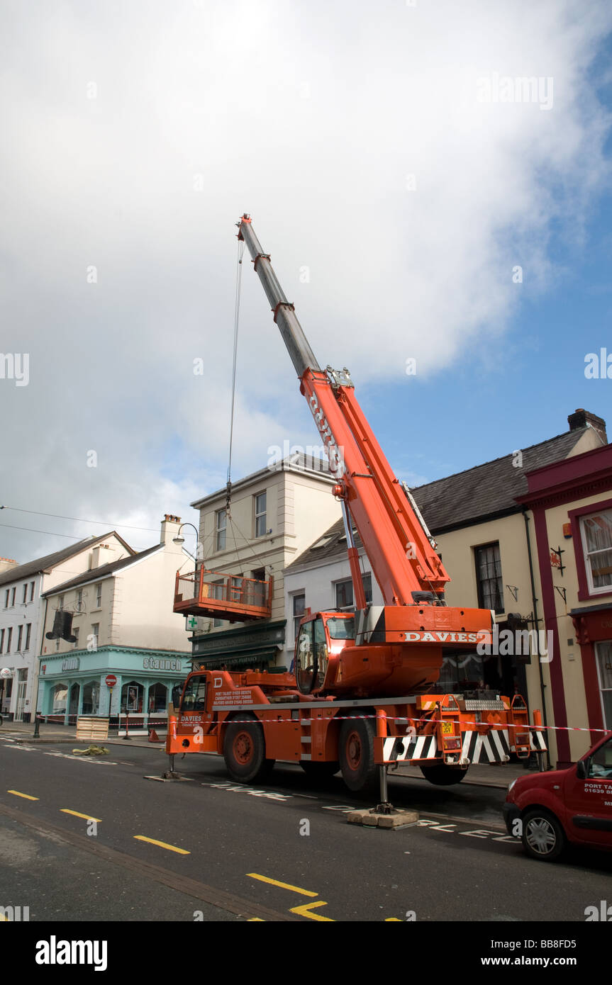 Large orange crane on carmarthen town centre lifting goods out of first floor property plant hire Stock Photo