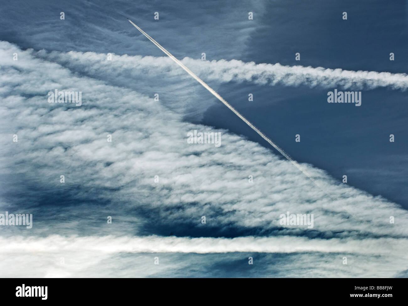 The jet trail from an aircraft  passing through other jet streaks from other planes Stock Photo