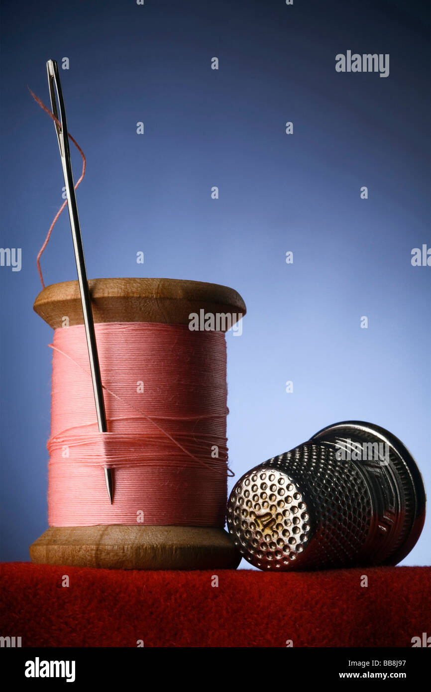 a wood spool of pink thread with the needle stuck in it and a thimble Stock Photo