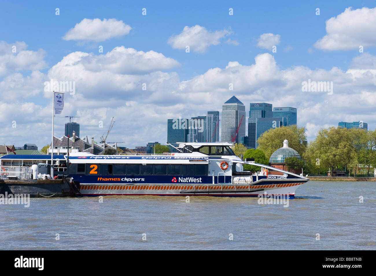 Greenwich pier with with river Thames Clipper catamaran passenger boat & dome of pedestrian tunnel & canary wharf in background Stock Photo