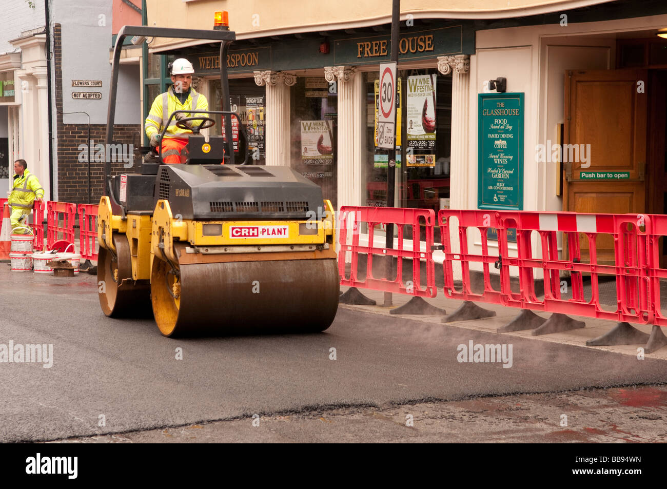 Man with PPE driving a road roller finishing off a newn peice of road Stock Photo