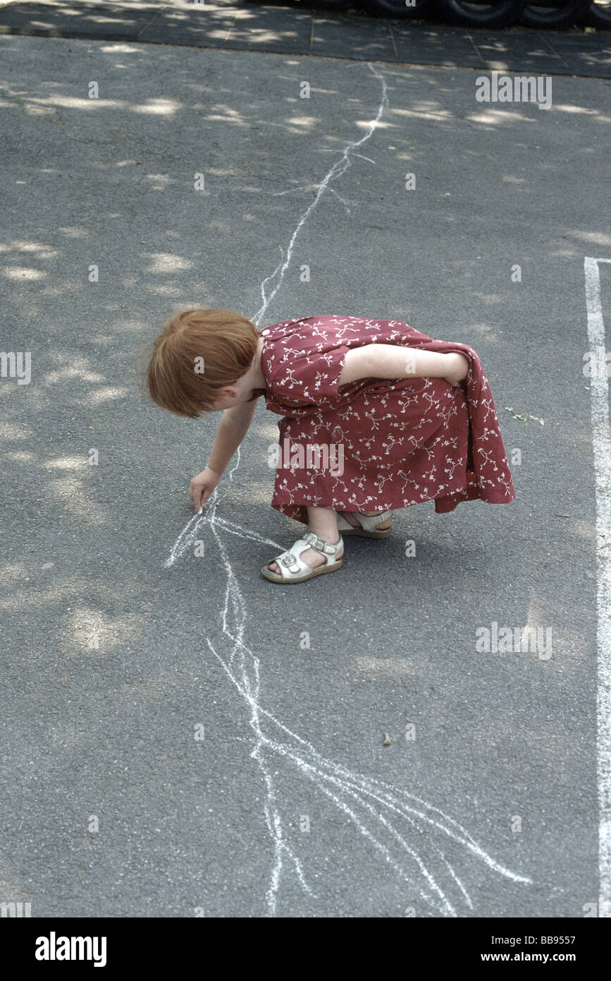 Primary school girl drawing on the school playground with white chalk Stock Photo