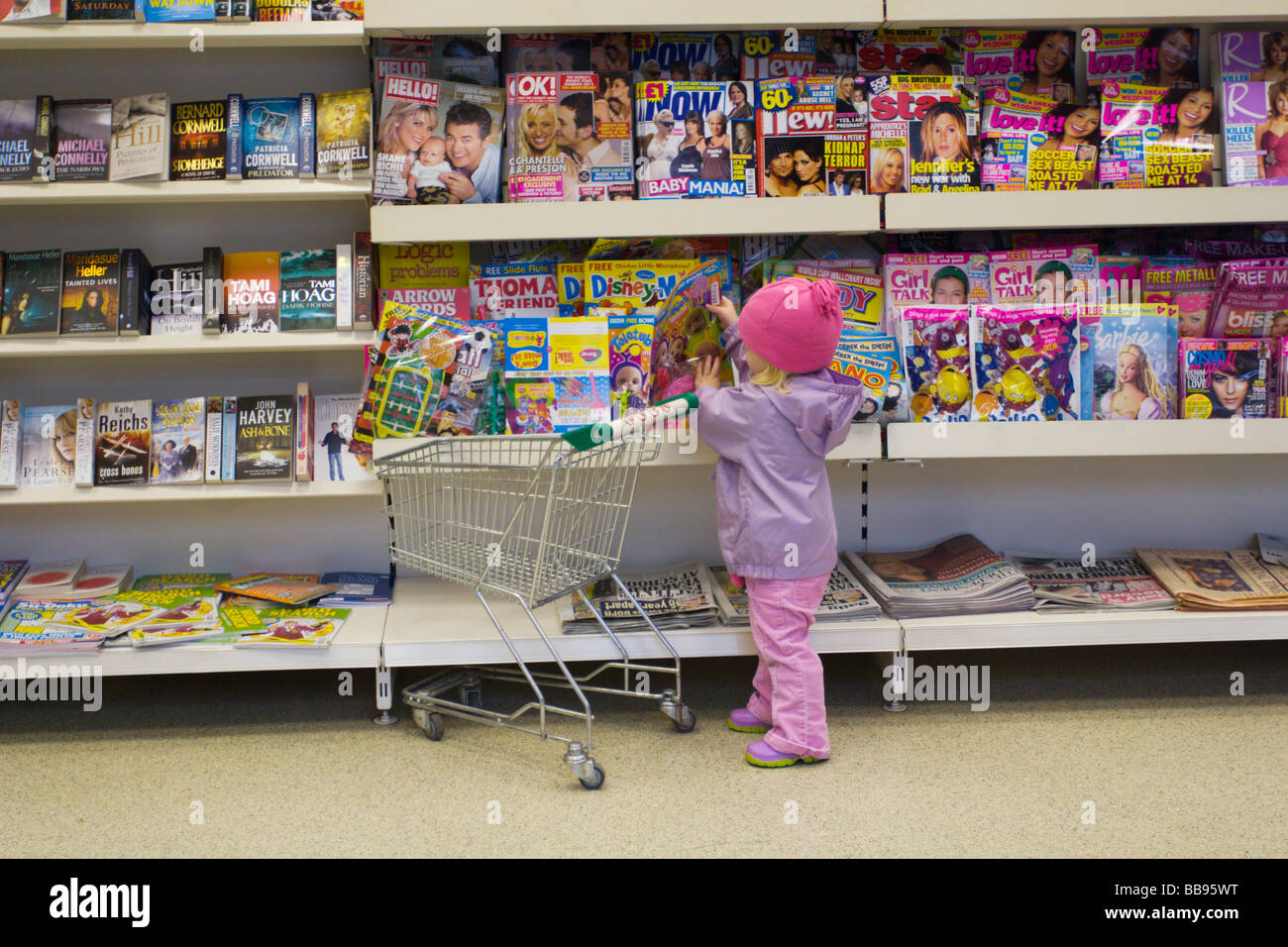 Child picking a teletubbies magazine from a magazine rack in a shop and putting it into a small shopping trolley. Stock Photo