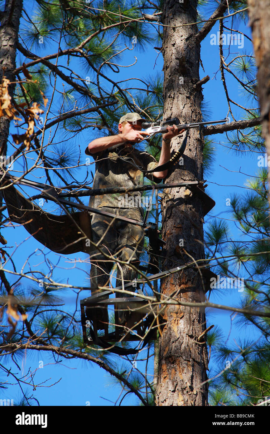 CLOSE UP HUNTER STANDING IN TREE STAND FIRING WEAPON HIGH IN A PINE