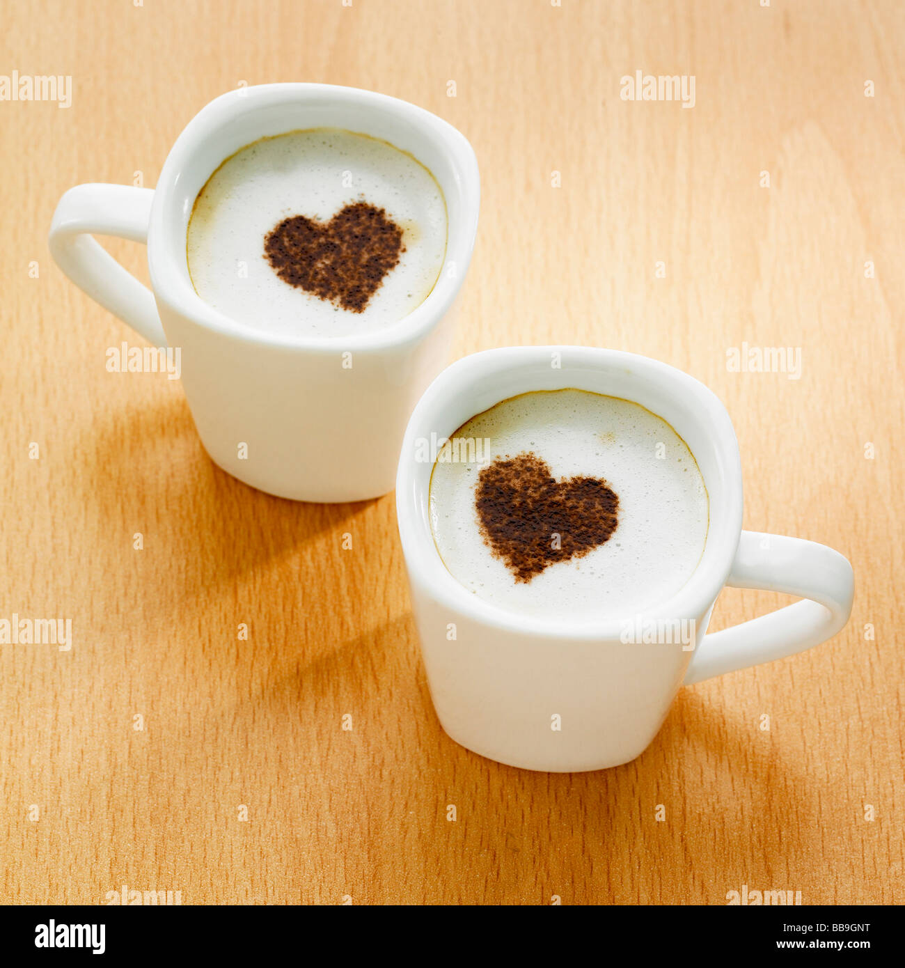 Two cups of coffee cappuccino style with heart shapes on the tops ...