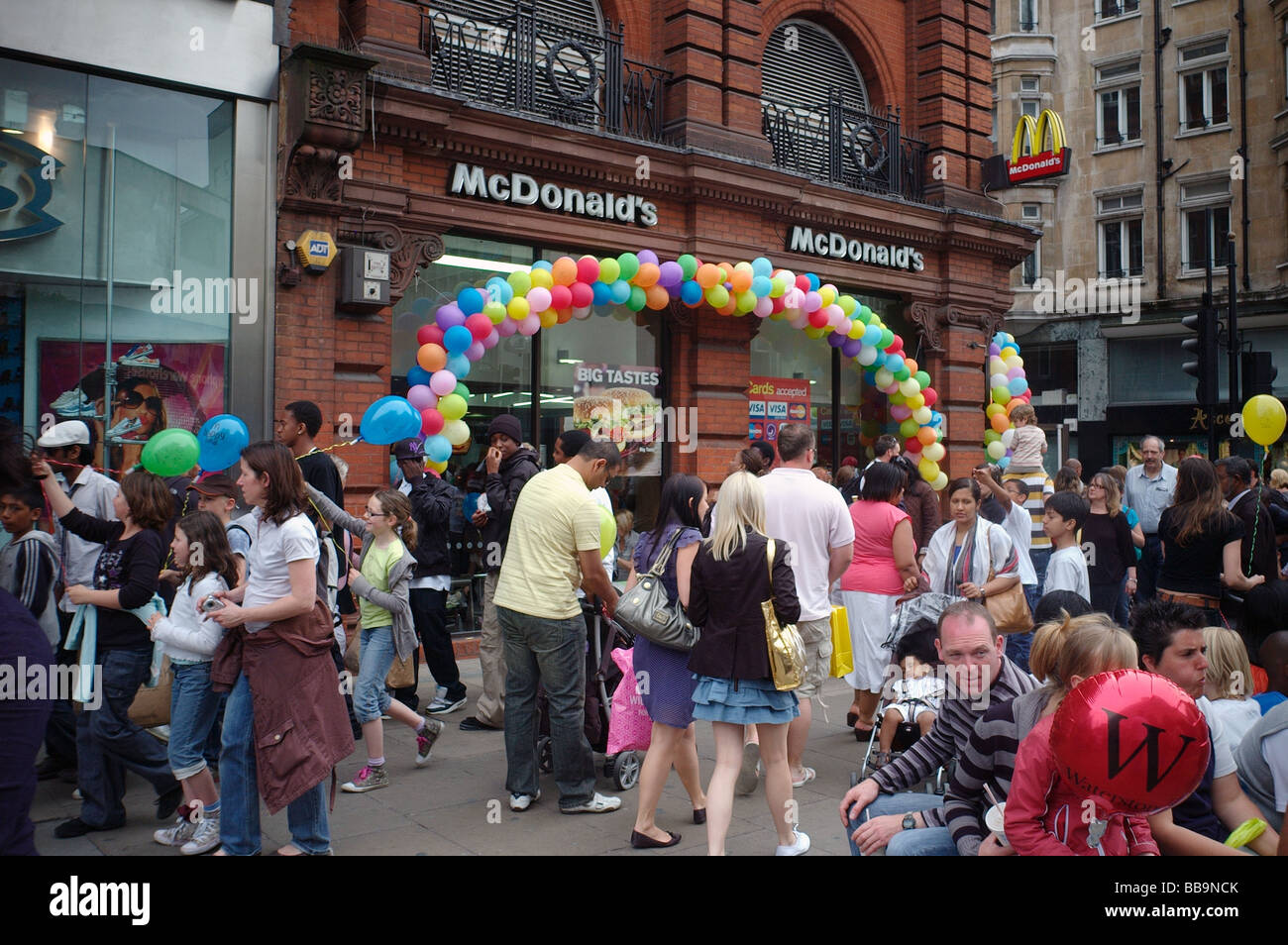 A crowd of people walking past a balloon festooned McDonalds on a