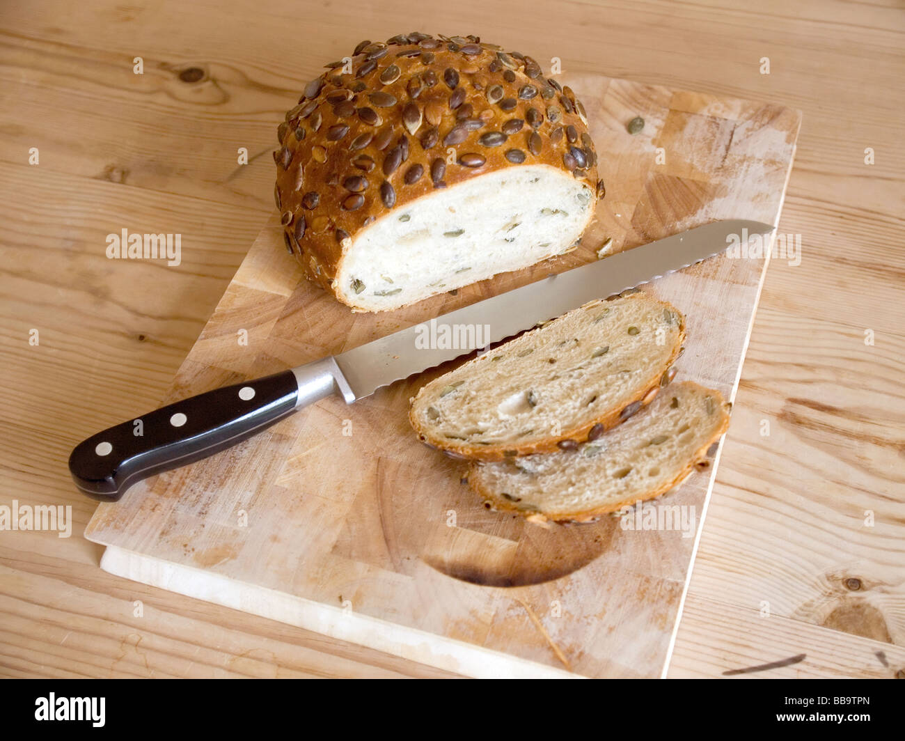 A newly sliced loaf of stone baked pumpkin seed loaf with a bread knife on a wooden board Stock Photo
