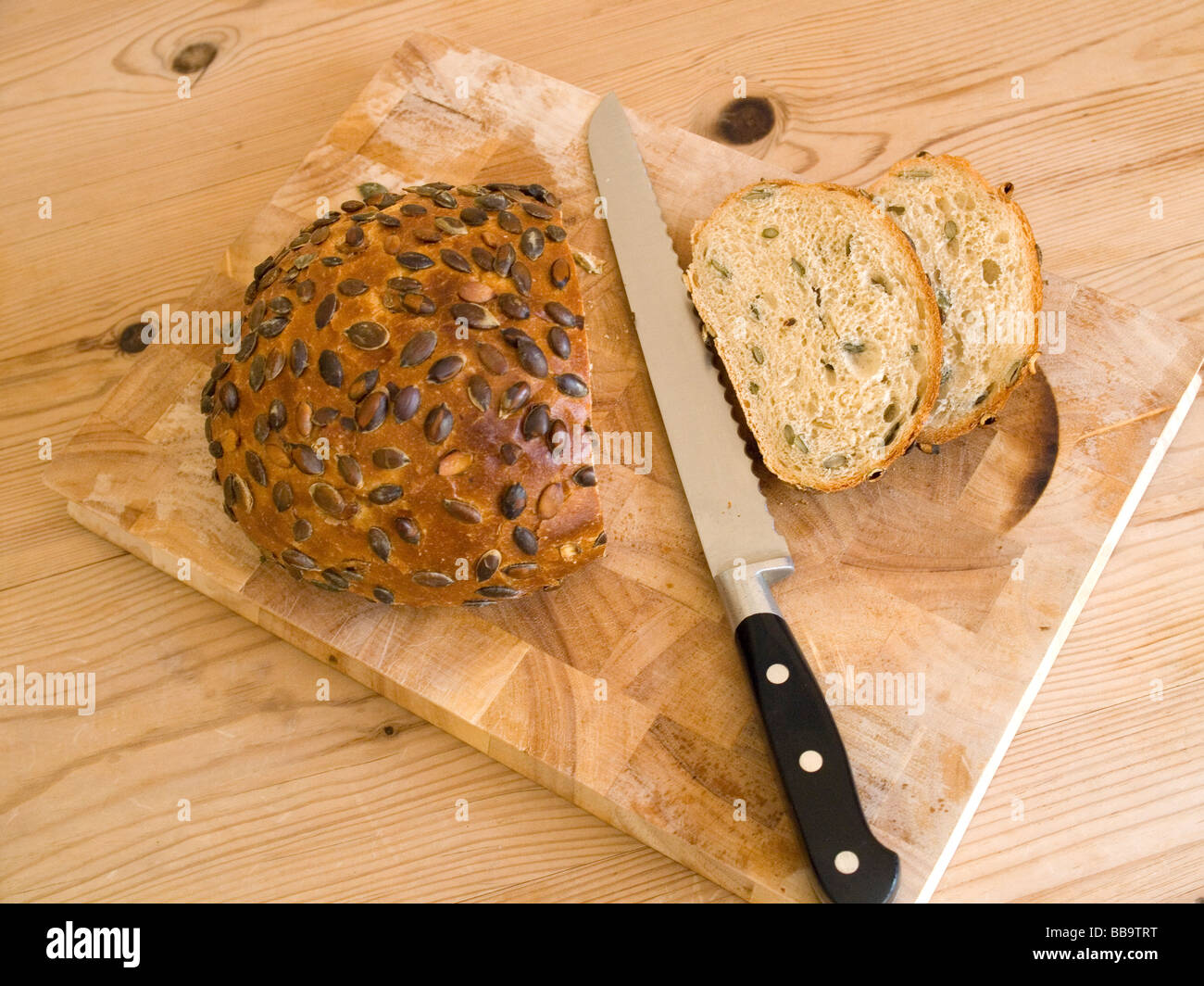 A newly sliced loaf of stone baked pumpkin seed loaf with a bread knife on a wooden board Stock Photo