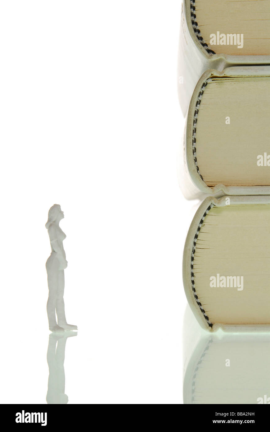 Miniature figure of a woman standing inquisitively in front of a stack of books, symbolic image for knowledge Stock Photo