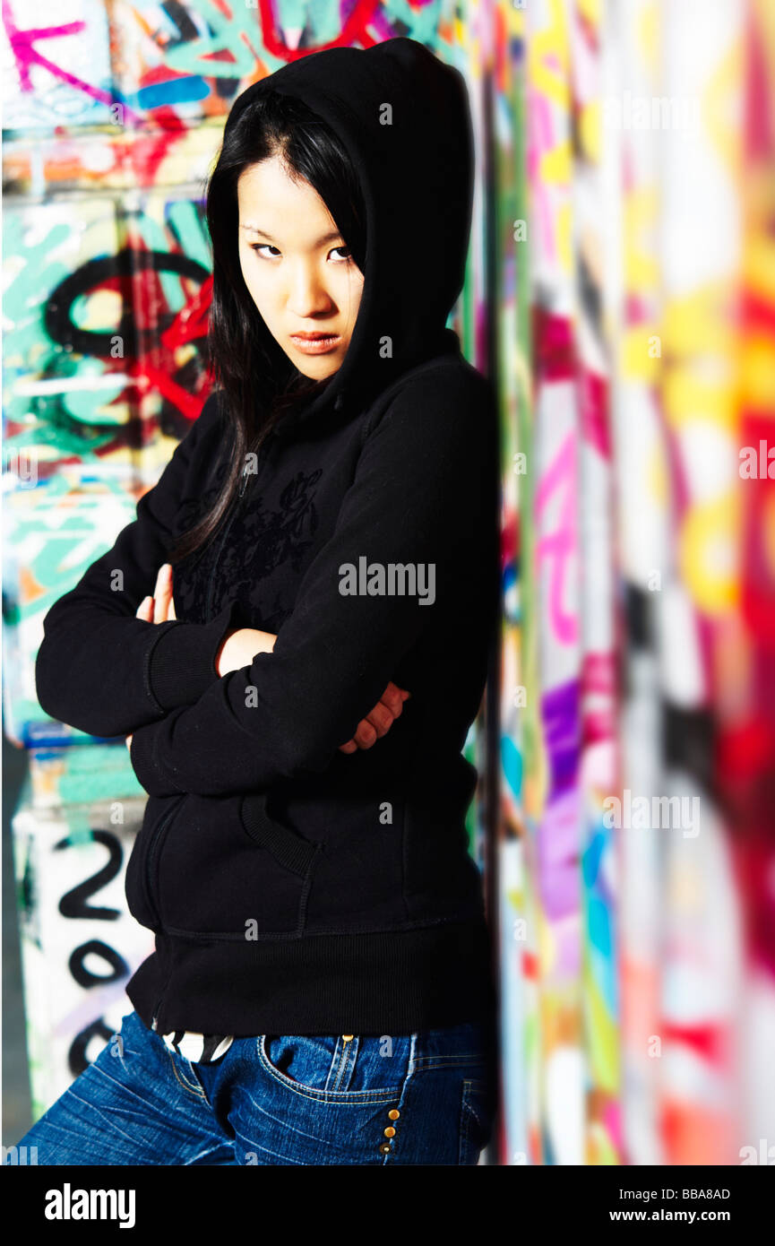 Young Asian girl in rapper pose in front of a wall with graffiti Stock Photo