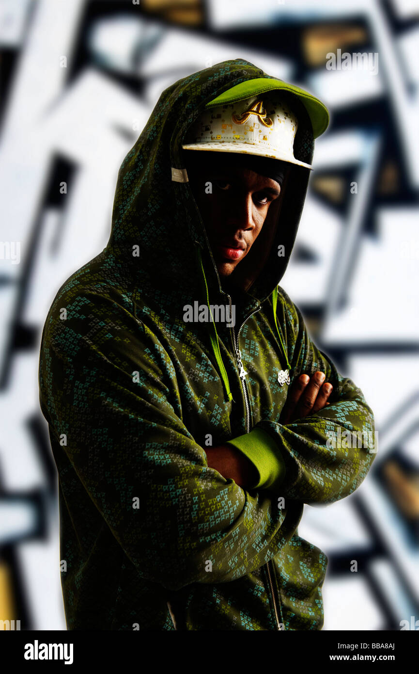 Dark-skinned young man in a rapper outfit in front of graffiti wall Stock Photo