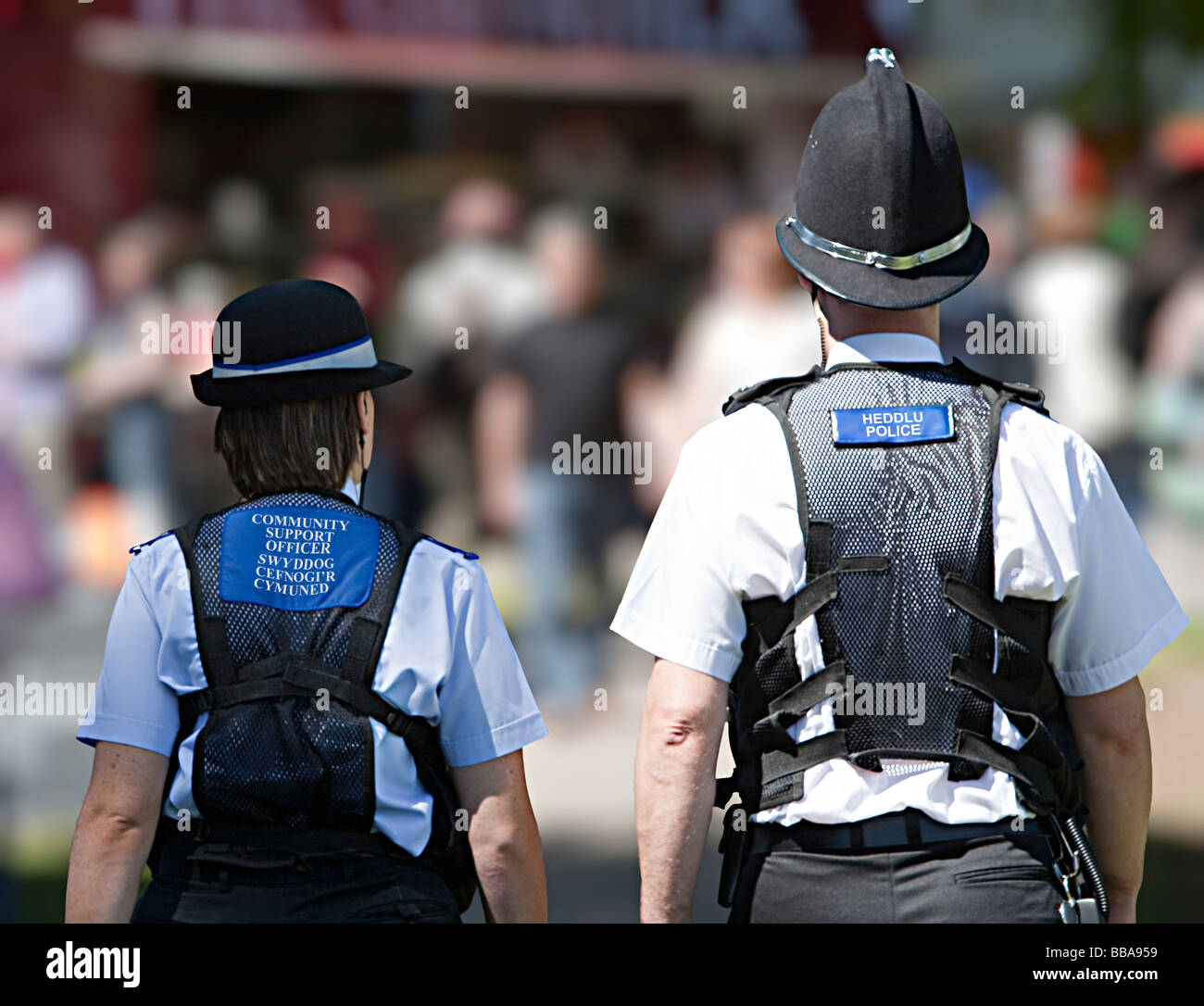 Community police officer with policeman walking through crowd at fair showing police labels in Welsh and English Wales UK Stock Photo