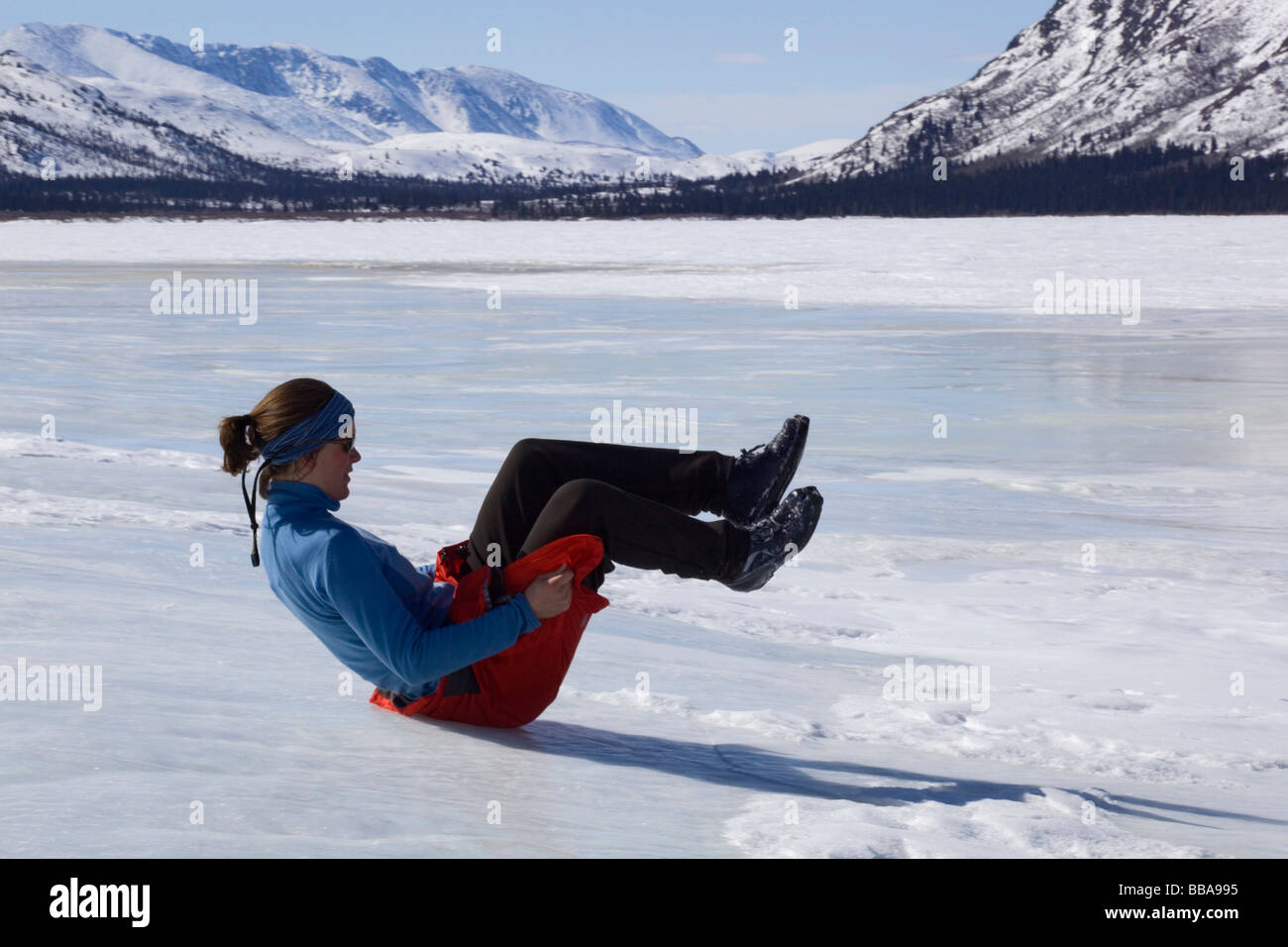 Woman playing, sliding down ice hill on her bottom, overflow, glaciation, ice building up on the shore of Fish Lake, spring, Yu Stock Photo