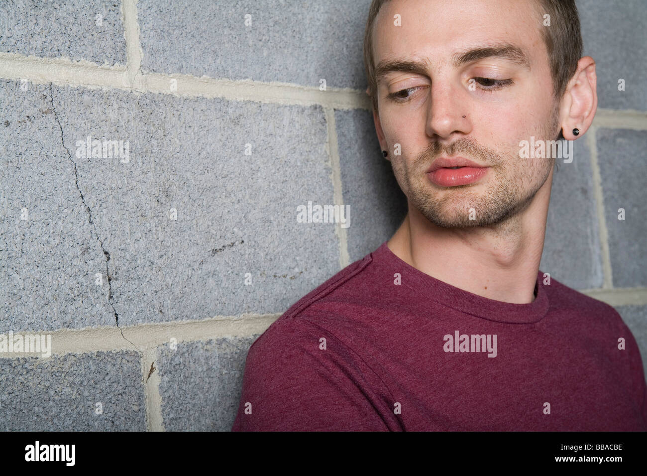 A young man leaning against a brick wall and looking away Stock Photo ...