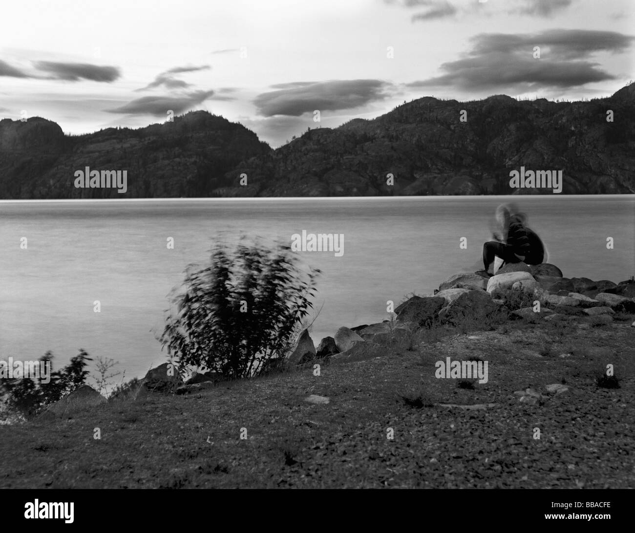 A person sitting at the edge of a lake Stock Photo