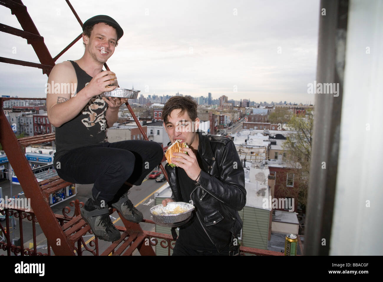 Two young men eating take out food on a fire escape Stock Photo