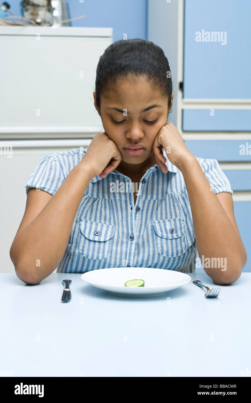 A young woman looking down at a slice of cucumber on a plate Stock Photo