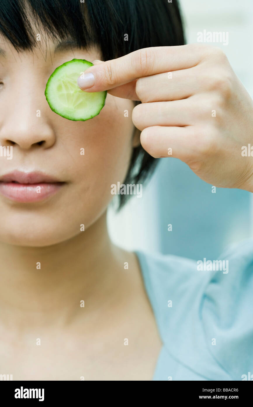 A woman holding a slice of cucumber in front of her eye Stock Photo