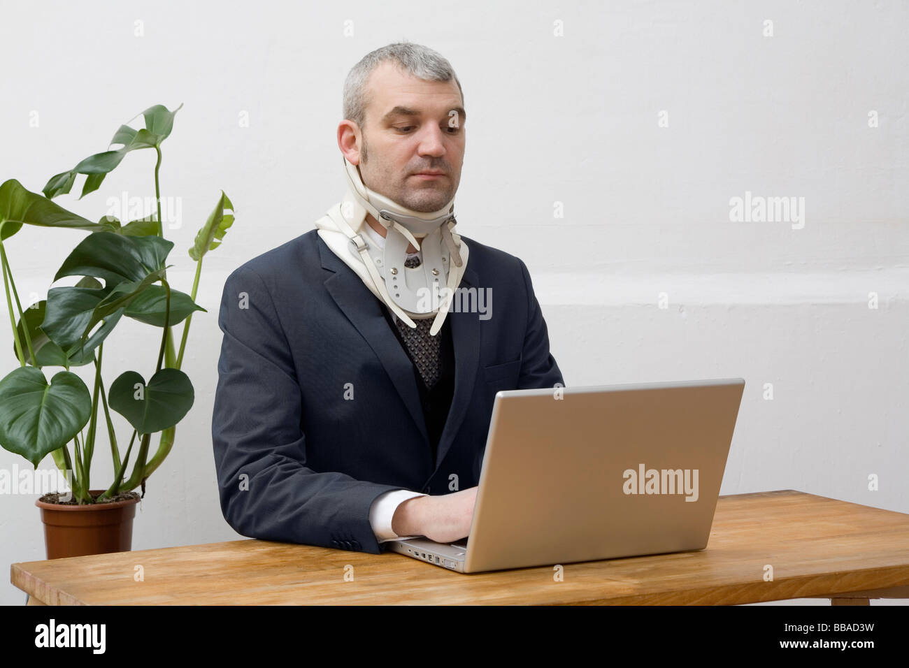 A businessman with a neck brace working on a laptop Stock Photo