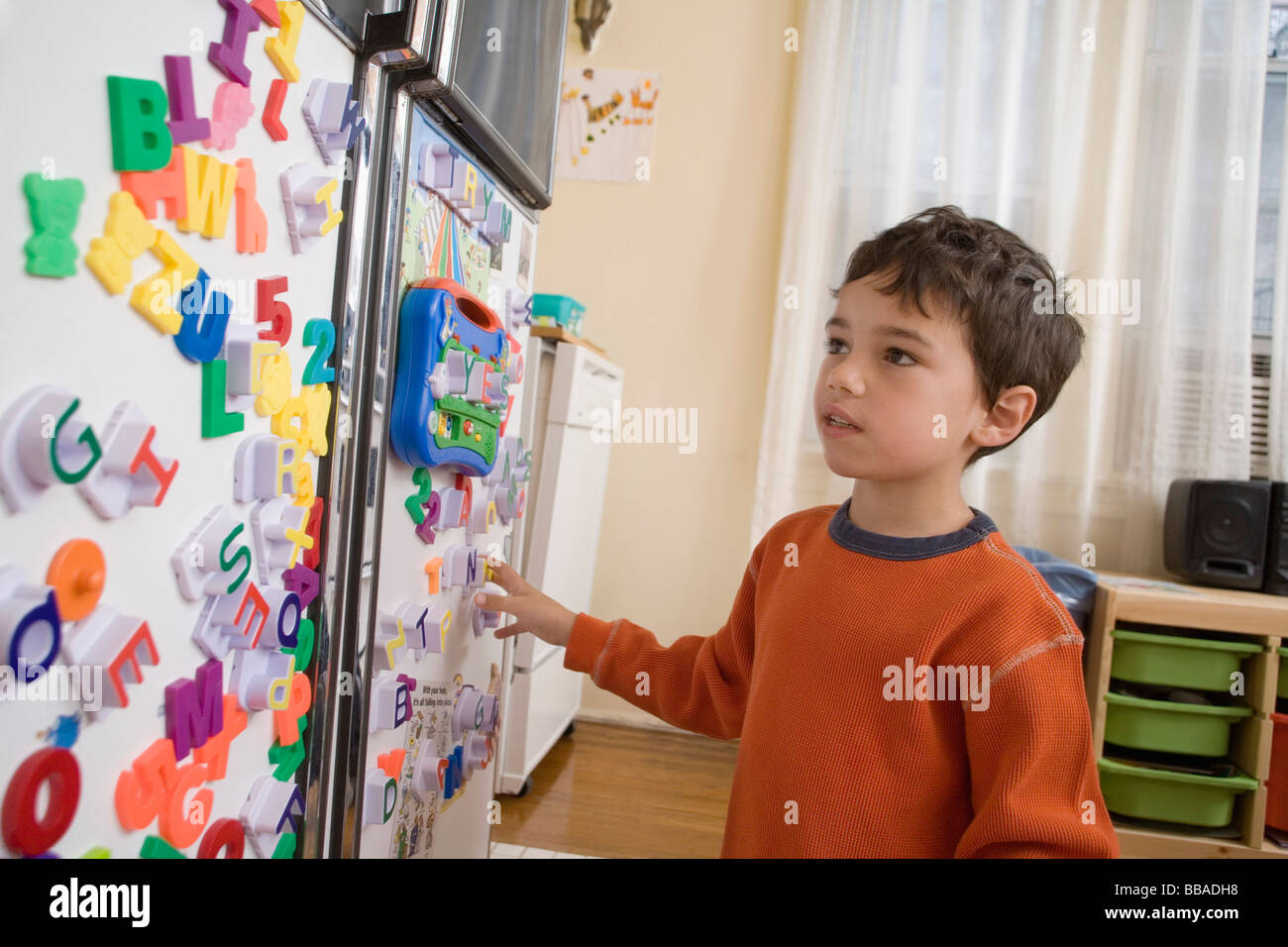 A young boy looking at toy magnets on a refrigerator door Stock Photo