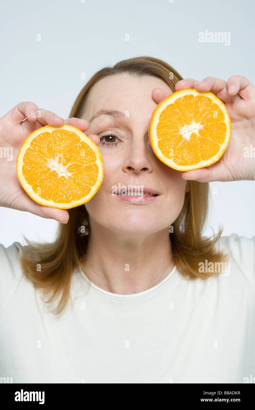 A woman holding two pieces of orange in front of her face Stock Photo ...
