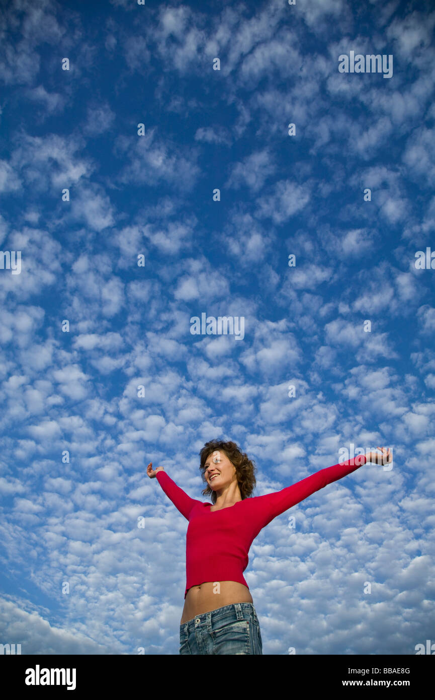 A woman with her arms raised against a cloudy sky, low angle view Stock Photo